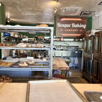 Bosque Baking Company - a baker working in a bakery - Inside Bosque Baking Company, shelves display various breads and baked goods, with kitchen appliances and workspaces visible in the background. - Bakeries Near Me - Albuquerque, New Mexico