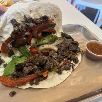 Dos Batos - Hybrid premium Taco - A sizable taco with a soft flour tortilla contains grilled beef, red and green peppers, onions, and lettuce, accompanied by a small cup of salsa on a metal tray. - Tacos Near Me - Austin, Texas