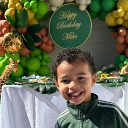 Birthday guest of honor standing in front of in front of one of the balloon decorations created by ABCister Events.