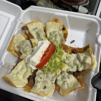 Santa Fe - a tray of nachos with cheese and sauce - A foam takeout container contains nachos with melted cheese, guacamole, sour cream, a tomato slice, and shredded beef, served as a Mexican snack or meal. - Mexican Near Me - Glen Ellyn, Illinois