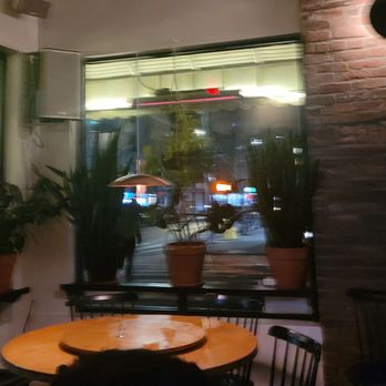 Win Son - A dimly lit restaurant interior features potted plants on the windowsill and a round wooden table with chairs, with a street view through the window. - Taiwanese Near Me - Brooklyn, New York