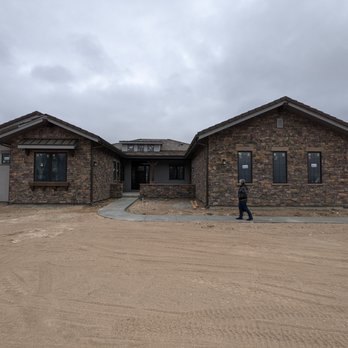 Sopris Homes - a man standing in front of a house - A modern, single-story house with brick and gray siding is under construction in a rural setting, with a person walking nearby. - General Contractors Near Me - Boulder, Colorado