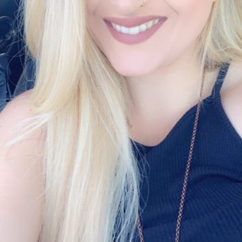 Rockit Hair Studio - What I had. - A woman with long, straight blonde hair, makeup including eyeshadow and lipstick, and a nose piercing is smiling at the camera. She is wearing a dark sleeveless top and a necklace, and appears to be sitting in a vehicle with a blurred background. - Hair Salons Near Me - Albuquerque, New Mexico