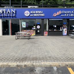 A storefront in a shopping plaza features signs for acai bowls, smoothies, and ice cream, with glass windows and a door, and outdoor seating.