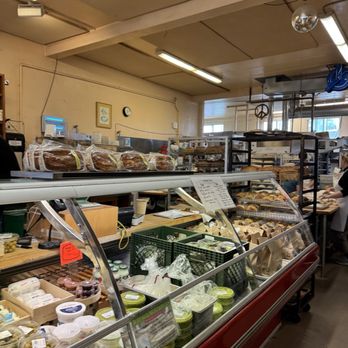 The Cheeseboard Collective - A bakery shop interior showing a glass display case with baked goods, cheeses, and other deli items, with bakery shelves and staff in the background. - Bakeries Near Me - Berkeley, California