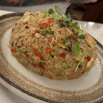 Fusionista - Fried Rice with shrimp - A serving of fried rice with shrimp, peas, carrots, and microgreens on a ceramic plate, with a tattooed arm visible in the background. - Peruvian Near Me - Montclair, New Jersey