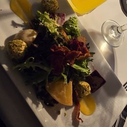 A mixed green salad with lemon wedges, garnished with various vegetables and possibly cheese or croutons, served on a rectangular plate.