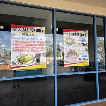 Senor Taco - Specials - The image shows two posters displayed in a restaurant window, promoting taco specials. The left poster offers a meal deal for $10.49, including soft drinks and various taco options, with an image of a taco plate. The right poster advertises Taco Tuesday with prices for hard shell beef tacos and street tacos, accompanied by images of the tacos. The window reflects the parking lot and trees outside, and the posters are framed by blue window panes. - Breakfast & Brunch Near Me - Phoenix, Arizona