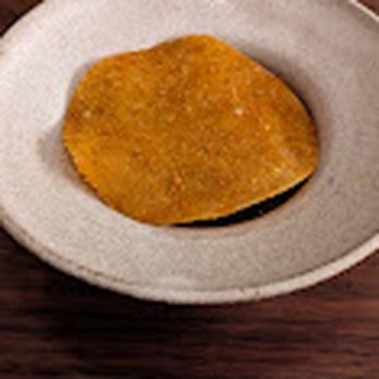 The Dabney - A fried item, possibly a croquette or similar snack, is placed on a small, white ceramic plate on a dark wooden surface. - New American Near Me - Washington, DC, District of Columbia