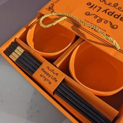 Gift box open and showing two small orange bowls and a set of chopsticks.