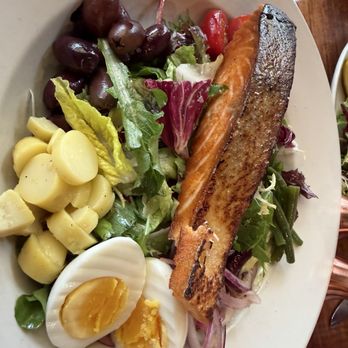 Zut On Fourth - Salmon Nicoise - A Salmon Nicoise salad featuring grilled salmon, boiled eggs, small potatoes, black olives, cherry tomatoes, and mixed greens on a white plate. - Mediterranean Near Me - Berkeley, California