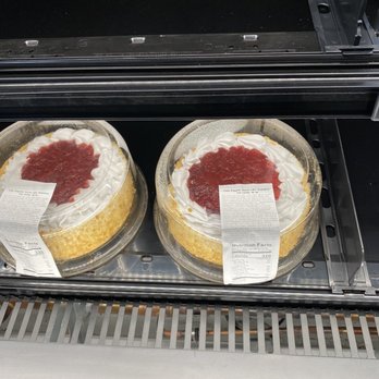 Amazon Fresh - Two round cakes with whipped cream and strawberry topping are displayed in a refrigerated case at a grocery store. - Grocery Near Me - Oceanside, New York