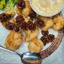 Walnut shrimp - A plate featuring fried shrimp topped with walnuts, accompanied by broccoli florets and a small bowl of creamy dipping sauce. The dish is presented on a decorative plate with a spoon nearby, suggesting a meal at Juicy Dumplings in Euless, TX, known for dumplings and walnut shrimp.