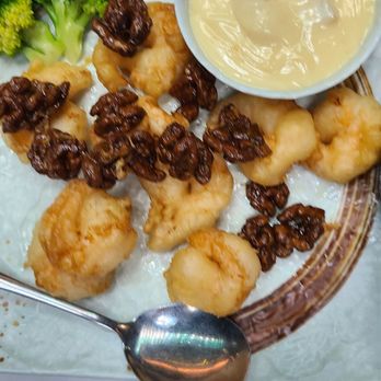 Juicy Dumplings - Walnut shrimp - A plate featuring fried shrimp topped with walnuts, accompanied by broccoli florets and a small bowl of creamy dipping sauce. The dish is presented on a decorative plate with a spoon nearby, suggesting a meal at Juicy Dumplings in Euless, TX, known for dumplings and walnut shrimp. - Chinese Near Me - Euless, Texas
