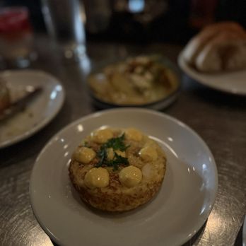Toro - A tapas dish served on a white plate features a round, fried item topped with dollops of yellow sauce and garnished with herbs, set on a dark wooden table. - Tapas Bars Near Me - Boston, Massachusetts