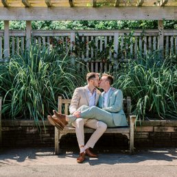 Grooms kissing on an outdoor bench in a garden Grooms kissing on an outdoor bench in a garden