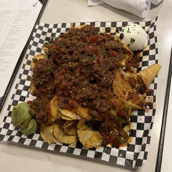 Highfields Restaurant & Eagle Landing Tavern - Loaded Nachos with Beef and Chorizo Chili - A plate of loaded nachos with beef and chorizo chili, served with sour cream and guacamole, on checkered paper at a restaurant. - New American Near Me - Jackson, New Hampshire