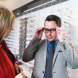 Photograph of a customer trying on glasses with the help of staff from Royal Oak Optometry.