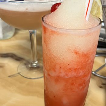Backyard Barbeque - A tall glass contains a frozen, blended red and white beverage garnished with a lemon wedge and a straw, likely a cocktail or mocktail. - Barbeque Near Me - Freeport, New York