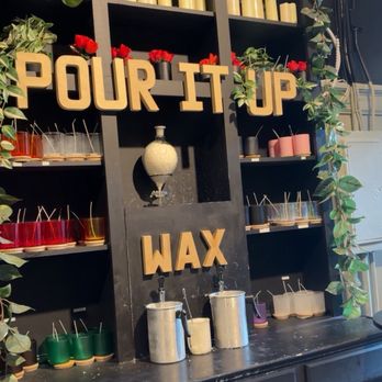 Scentique - Wax walll - A black shelving unit decorated with candles, plants, and wax products at Scentique in Providence, RI, with a sign reading 'POUR IT UP WAX.' - Customized Merchandise Near Me - Providence, Rhode Island