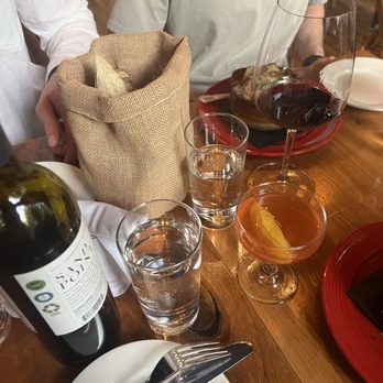 Amelie - Bread and paper plane - A dining table with wine glasses, water glasses, a bottle of wine, a bread basket, and plates, set in a restaurant environment. - Wine Bars Near Me - Washington, DC, District of Columbia