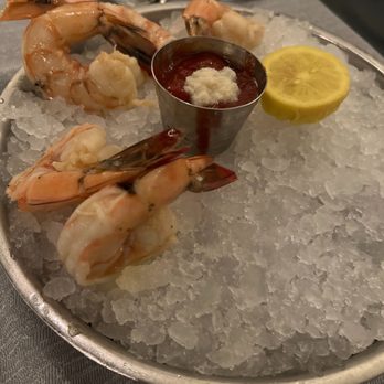 PY Steakhouse - Guaymas Shrimp Cocktail - A seafood dish featuring cooked shrimp on crushed ice, accompanied by lemon slices and cocktail sauce in a metal cup. - Steakhouses Near Me - Tucson, Arizona