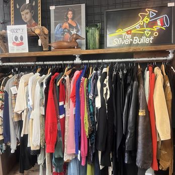 Casa - Vendor space at Casa LB. - A clothing rack displays a variety of vintage and secondhand garments, including shirts, jackets, and dresses, in a thrift store. The background features decorative items and framed artwork. - Antiques Near Me - Long Beach, California