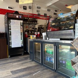Interior - The image shows the inside of a coffee shop featuring a glass display case, beverage refrigerators, and a menu board with drink options.