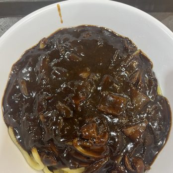 Young Chow Loo - Jjajang Noodle - A bowl of noodles covered with a dark, glossy sauce containing chunks of meat or vegetables, served in a white dish. - Korean Near Me - Burlington, Massachusetts