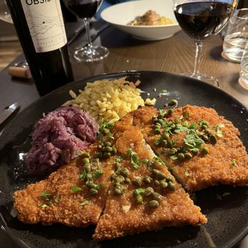 Alsace - Schnitzel - A dish featuring breaded schnitzel topped with capers, accompanied by mashed potatoes and sauerkraut, on a black plate at a restaurant. - French Near Me - Union, Maine
