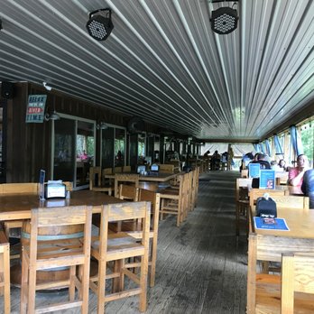 Rustic River Restaurant - Outside dining - The image shows an outdoor dining area at Rustic River Restaurant, with wooden tables and chairs arranged along a deck. Large windows and open sides provide views of the Powell River, and the ceiling is made of metal panels with mounted lighting. Several patrons are seated, enjoying the view and the atmosphere. The setting combines rustic decor with natural surroundings, suitable for outdoor dining. - American Near Me - Tazewell, Tennessee