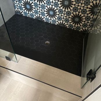 The Groutsmith - This image showcases a modern shower with a dark hexagonal tile floor and a striking patterned wall featuring black and blue ... - Grout Services Near Me - Sarasota, Florida