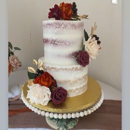 Wedding Cake Cupcake - A two-tier wedding cake with a semi-naked frosting style, decorated with roses, dried flowers, and berries, placed on a gold cake board.