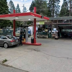A clean and well-maintained gas station with a convenience store, easy parking, fuel pumps, and a beautiful forest backdrop.