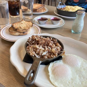 The Harvest Room - Hash and Eggs - A breakfast meal includes hash with eggs, toast, and beverages like water and soda, served on a wooden table. - New American Near Me - Munster, Indiana