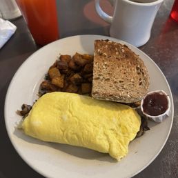 Sir Charles Omelette - A breakfast plate includes a yellow omelette, toasted bread, roasted potatoes, and a small cup of jam, with a glass of orange juice and a coffee mug nearby.