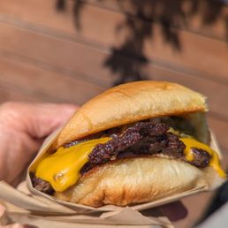 Single patty - A cheeseburger featuring a beef patty, melted cheddar cheese, and crispy bacon in a soft bun, held outdoors.