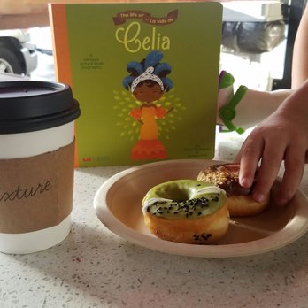 Local Fixture - Medium mocha latte, Lil' Libros Celia book, matcha and poppy seed donut, s'mores donut and eager little hand ready to devour donut! - Gift Shops Near Me - Whittier, California Local Fixture - Medium mocha latte, Lil' Libros Celia book, matcha and poppy seed donut, s'mores donut and eager little hand ready to devour donut! - Gift Shops Near Me - Whittier, California