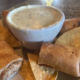 Spinach Dip! - A plate featuring a bowl of creamy spinach dip surrounded by tortilla chips and taquitos, served on a restaurant table.
