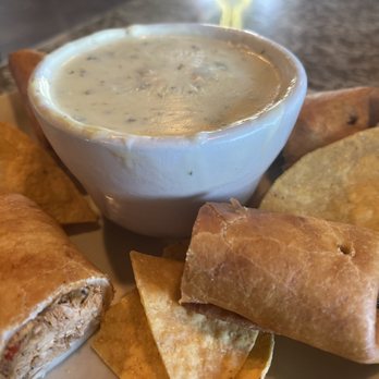 El Rodeo - Spinach Dip! - A plate featuring a bowl of creamy spinach dip surrounded by tortilla chips and taquitos, served on a restaurant table. - Mexican Near Me - Clive, Iowa