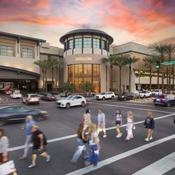 Shoppers cross the street outside Hermès at Scottsdale Fashion Square under a colorful sunset sky.