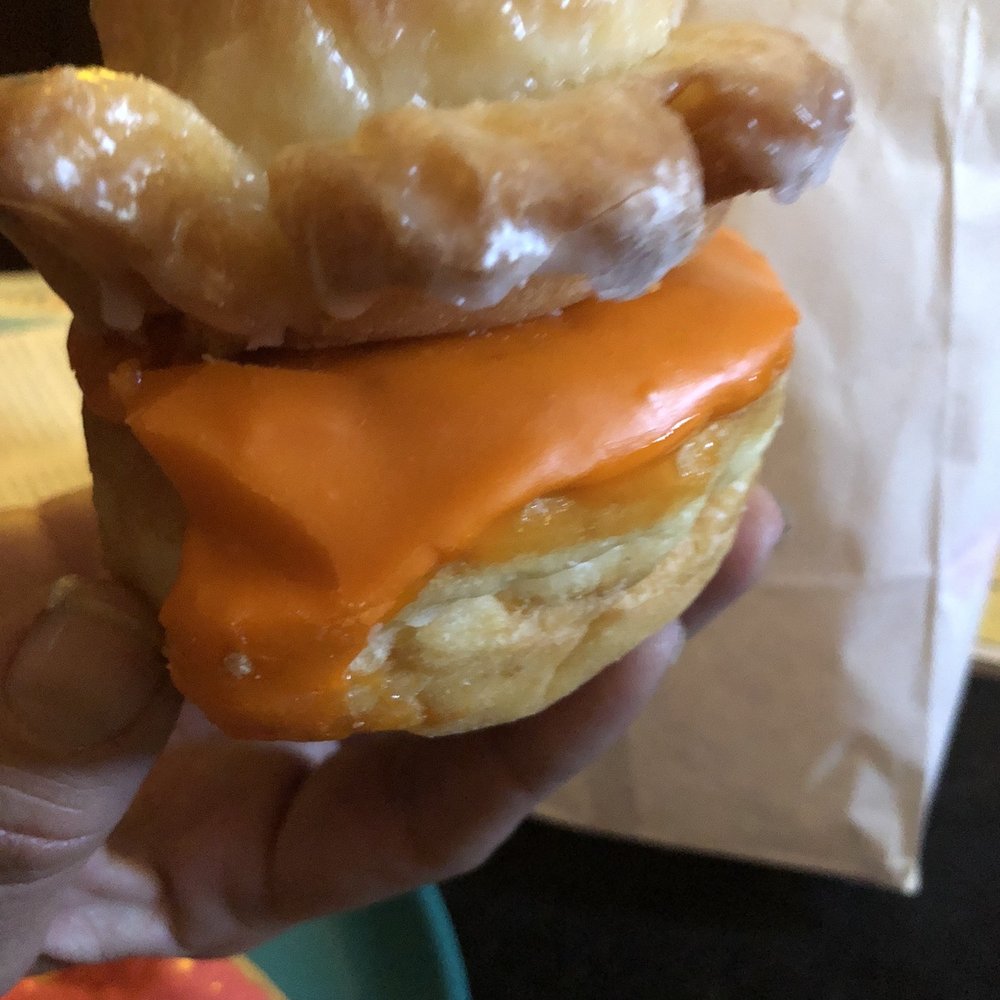 Golden West Donuts - a hand holding a glazed donut with orange icing - Donuts Near Me - Norwalk, California Golden West Donuts - a hand holding a glazed donut with orange icing - Donuts Near Me - Norwalk, California