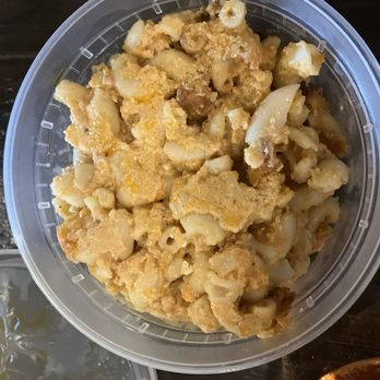 Texas Steele BBQ - Mac and Cheese - A clear plastic container holds macaroni and cheese with a creamy, cheesy sauce and cooked pasta, placed on a dark surface. - Food Trucks Near Me - Columbus, Ohio