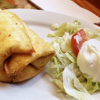 Cielito Lindo - Chicken Chimichanga - A golden-brown chicken chimichanga is placed on a white plate, accompanied by a side salad with lettuce, tomato, and sour cream. - Mexican Near Me - Milwaukee, Wisconsin