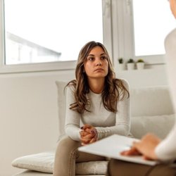 Connections Wellness Group - A woman sitting on a couch listening to a counselor holding a clipboard, illustrating a counseling or therapy session.