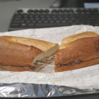 Cafe Primavera - The "New Yorker" - grilled roast beef and provolone on a garlic toasted roll. Outstanding! - A sandwich with sliced roast beef and melted provolone cheese inside a garlic toasted roll. The sandwich is cut in half, showing the filling, and is placed on a piece of wax paper. The background includes a computer keyboard, indicating an indoor setting. - Italian Near Me - Poughkeepsie, New York