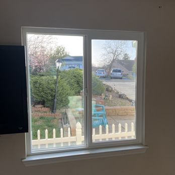 High Performance Roofing - New window - A window view of a garden with bushes, a lamppost, and a fence, along with parked cars and houses on the street. - Roofing Near Me