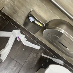 Nasty women's bathroom w/ used feminine products on the floor and overflowing from the bin