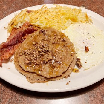 Huckleberry's - Pumpkin pancake special with over easy egg, bacon and hash browns. - A breakfast plate featuring hash browns, a fried egg, crispy bacon, and a stack of pancakes topped with syrup and crushed nuts. - Breakfast & Brunch Near Me - Modesto, California