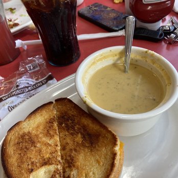Friendly's - What I actually was served. - A breakfast plate includes a toasted grilled cheese sandwich with golden-brown bread, served alongside a bowl of creamy, seasoned soup with a spoon inside. A large glass of dark soda with ice and a straw is also visible on the red table, along with condiments and a smartphone. The setting appears to be a casual restaurant or diner. - Ice Cream & Frozen Yogurt Near Me - Commack, New York